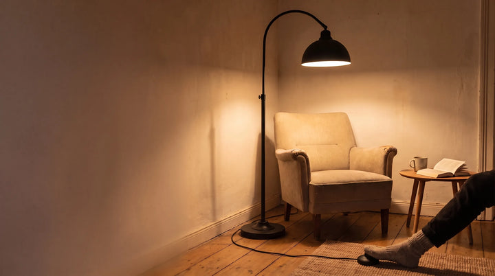 Fuß bedient den Schalter einer schwarzen Bogen-Stehlampe mit warmem Licht in gemütlicher Leseecke