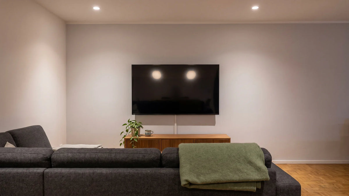 Dunkler Wandfernseher im Wohnzimmer, in dem sich zwei Deckenspots als helle Punkte spiegeln